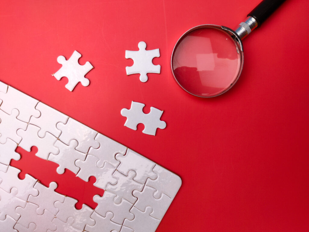 Magnifying glass searching missing puzzle on red background